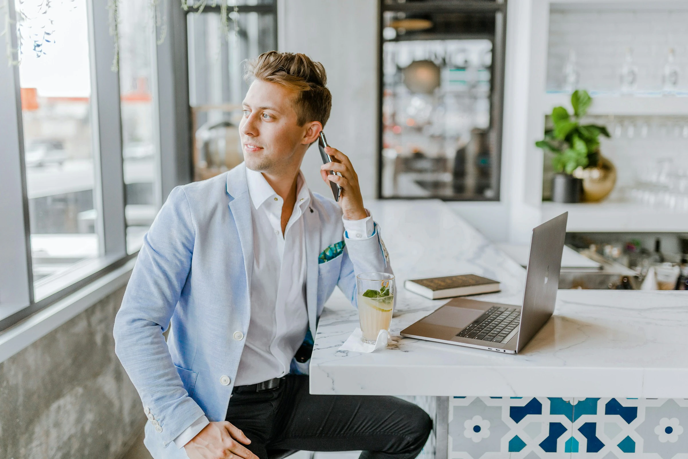 An agent on the phone by the window, laptop in front of him